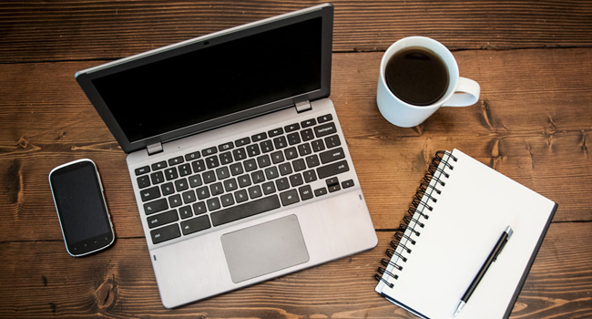 Computer on desk with phone, coffee and notepad.