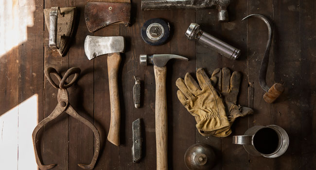 Tools laid out on a table: hammer, axe, pocket knife, measuring tape, etc.